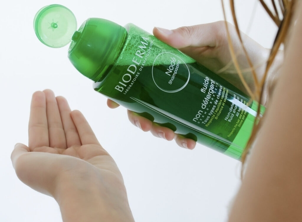 Personne utilisant le shampooing Bioderma Nodé vert.