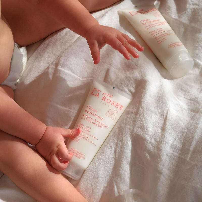 Bébé avec crème hydratante bio sur lit blanc.